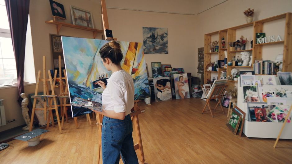 A dedicated artist working on a colorful canvas in a bright, organized studio.